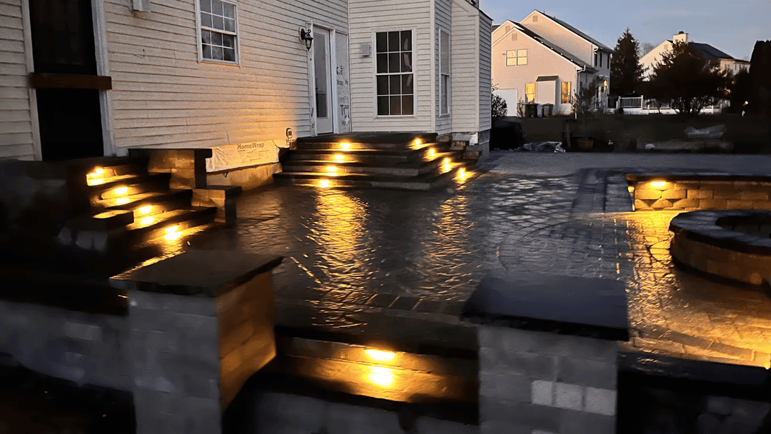 Outdoor patio with illuminated stone steps and paved area, showcasing modern landscape lighting.