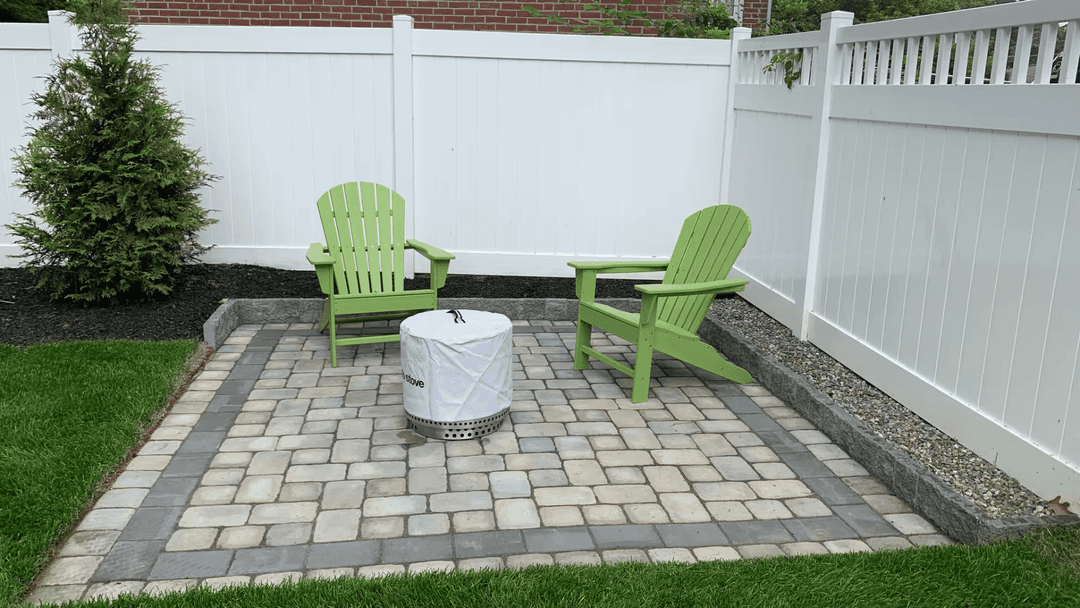 Garden patio with green chairs and a fire pit, surrounded by a white fence and grass.