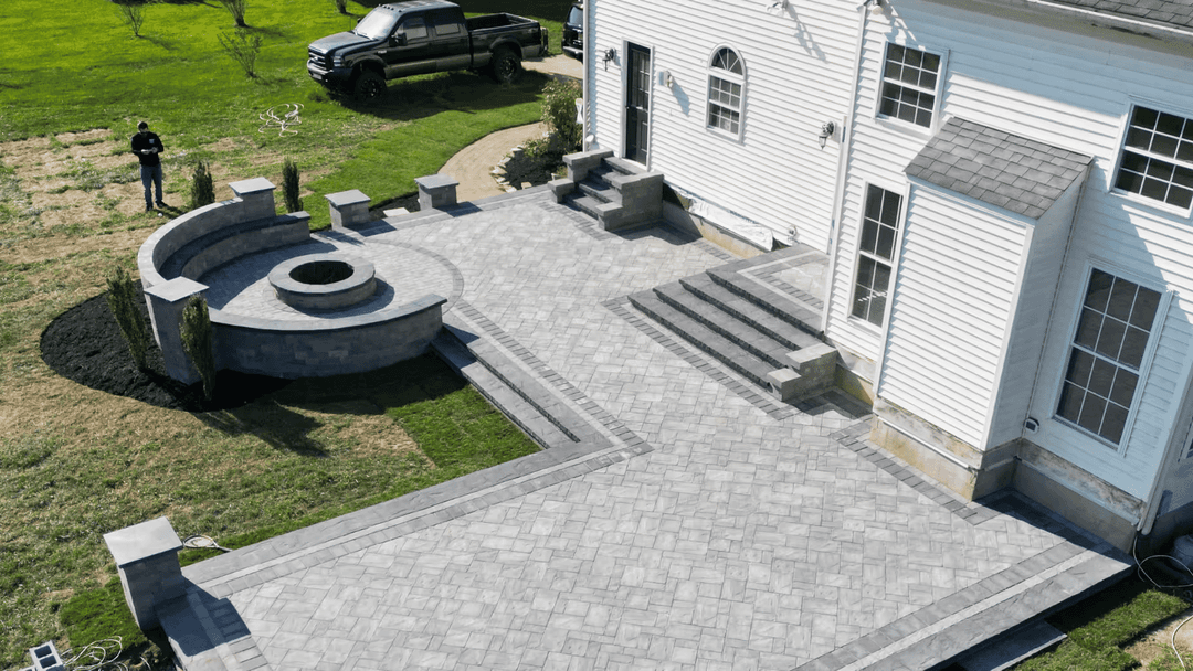 Aerial view of a paved patio with a fire pit and landscaping in a residential backyard.