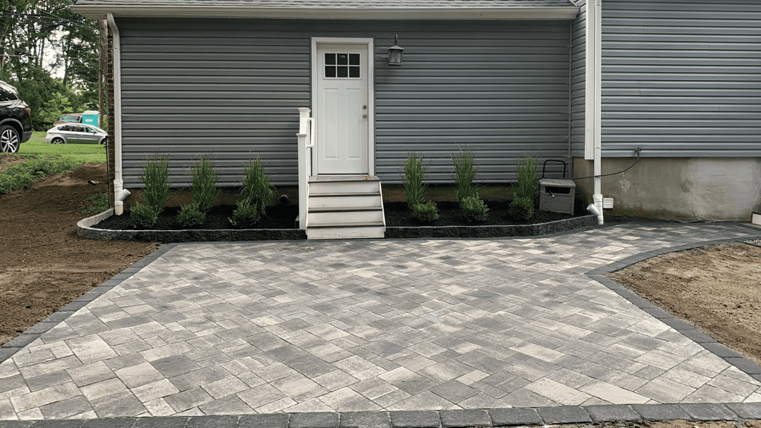 Newly installed paver patio with steps and landscaped garden by a gray house.