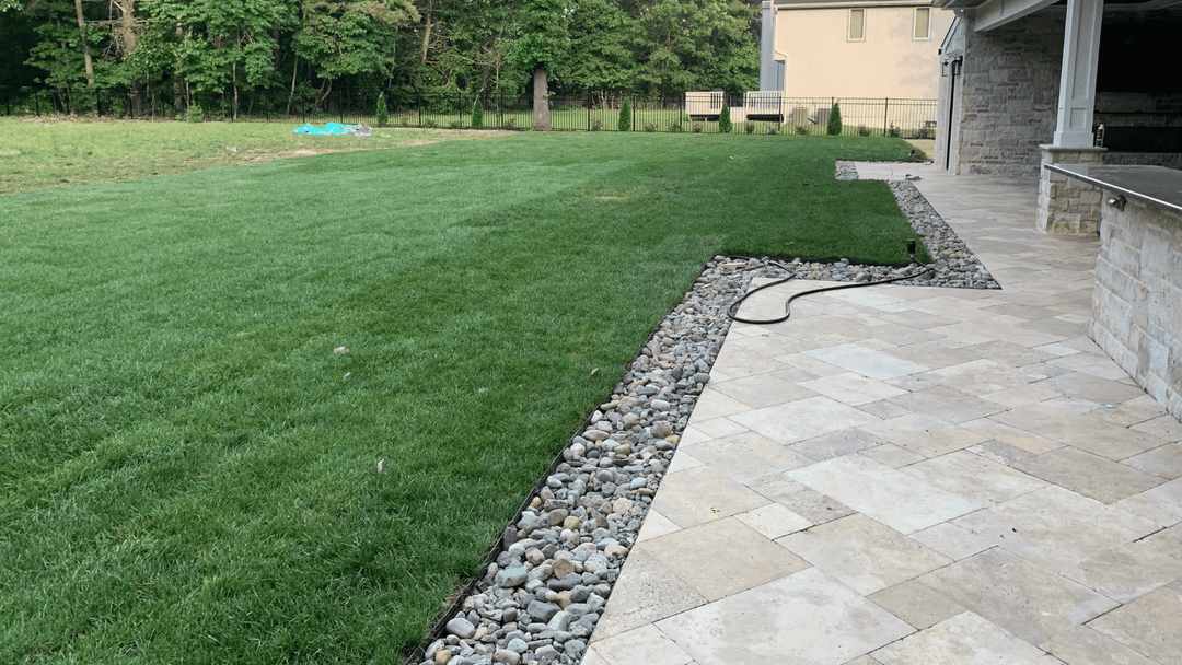 Lush green lawn with stone border and patio area beside a modern home.