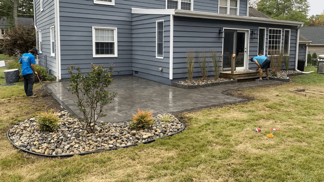Home exterior renovation with new paver patio, landscaping, and workers installing features.