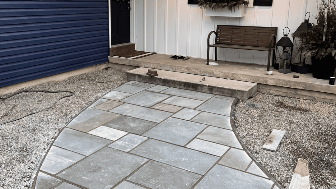 Curved stone walkway leading to a home with a bench and decorative plants.