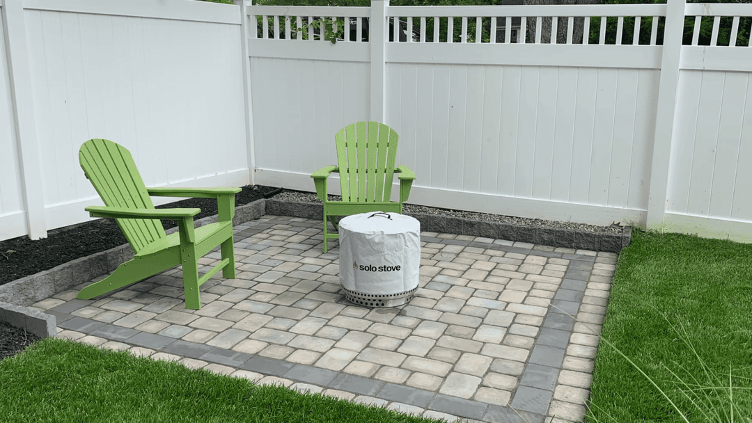 Outdoor seating area with green Adirondack chairs and a Solo Stove fire pit on a stone patio.
