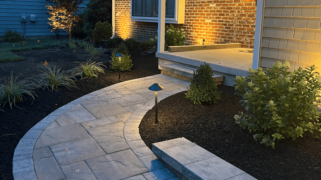 Illuminated walkway and landscaped garden at night by a modern home entrance.