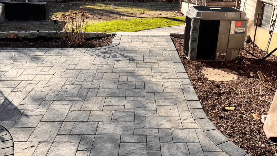 Paved patio with gray stone design and landscaping featuring mulch and greenery.