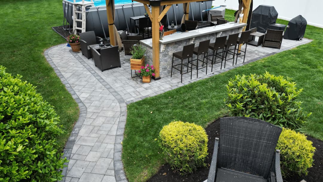 Backyard patio with bar, seating, and landscaped greenery, featuring a pool and stone pathway.