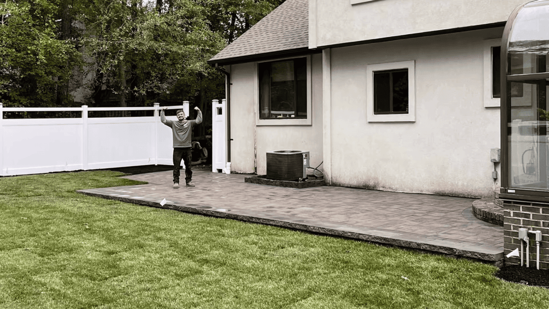 Person celebrating on a newly paved patio in a backyard with a white fence and green lawn.