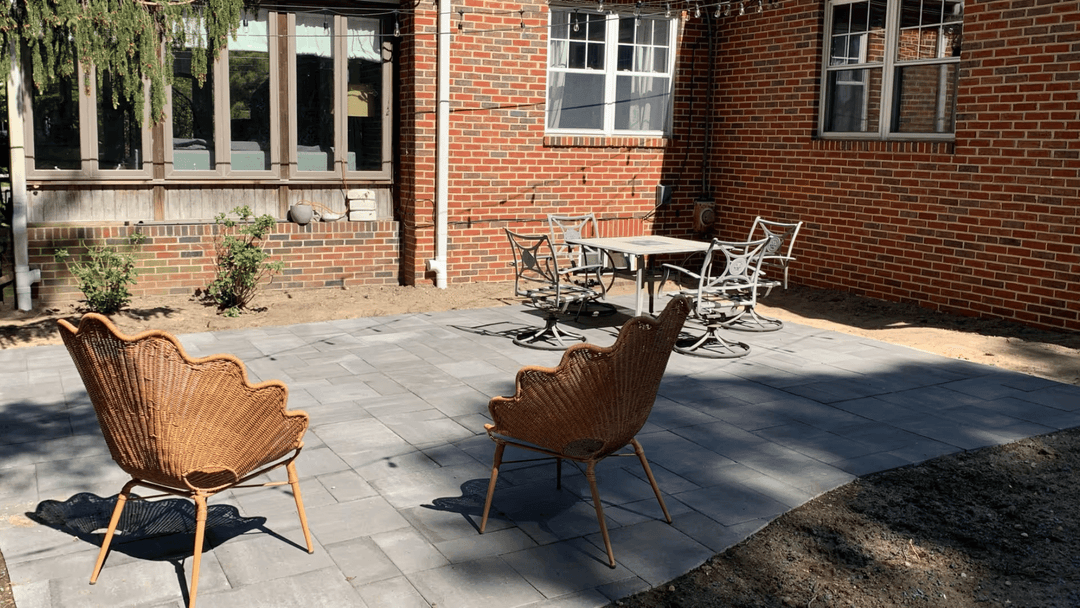 Cozy backyard patio with rattan chairs and a dining table, surrounded by brick walls and greenery.
