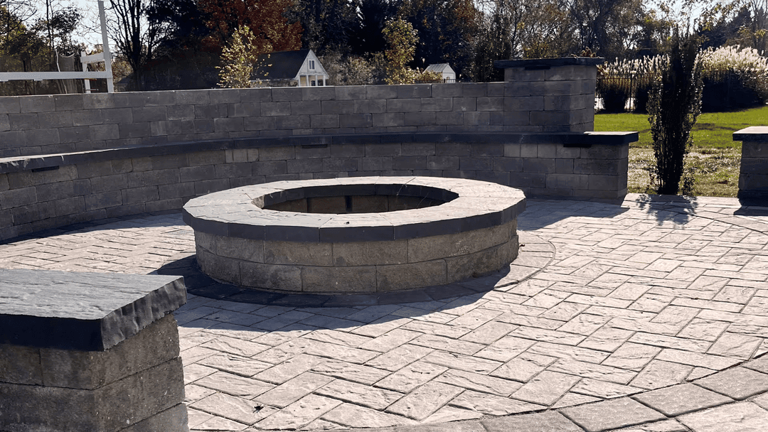 Outdoor stone fire pit surrounded by a circular seating wall in a landscaped backyard.