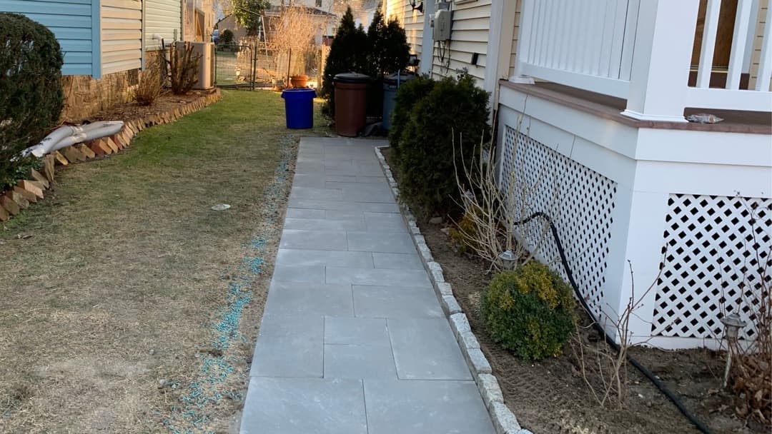 Bluestone pathway bordered by grass and shrubs, leading alongside homes.