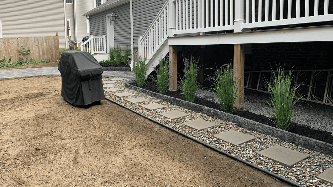 Backyard with stone pathway, grill, and decorative grasses near a raised deck.