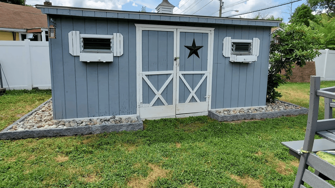 Gray backyard shed with white doors, star decoration, and grassy surroundings.