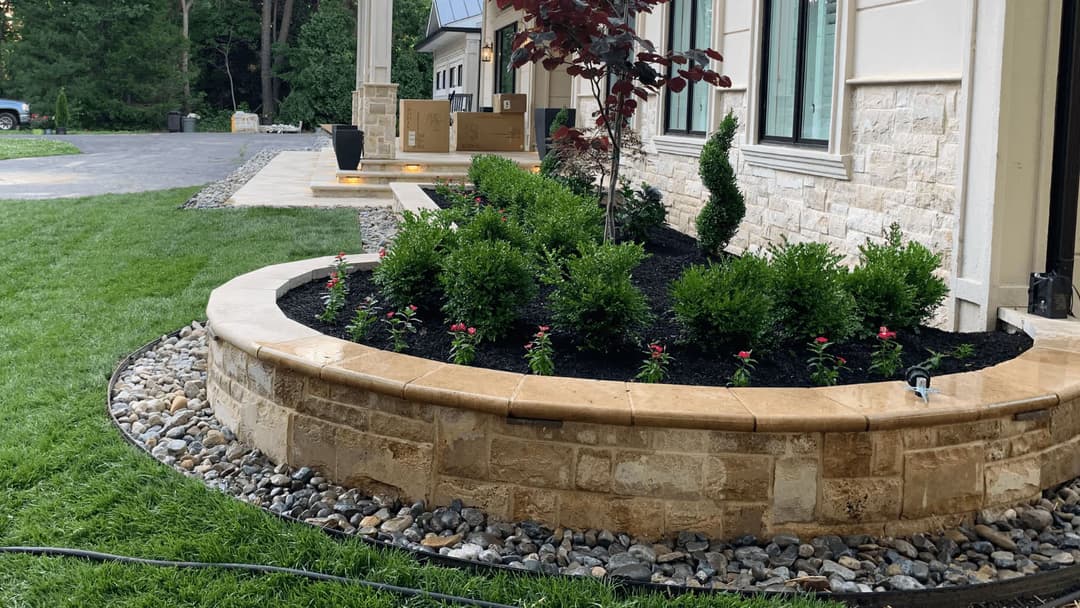Landscape design featuring curved stone planter, lush green shrubs, and flowering plants.