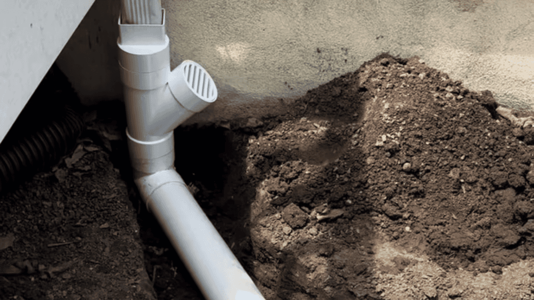 White PVC drain pipe installed in soil with surrounding dirt, showcasing drainage system setup.