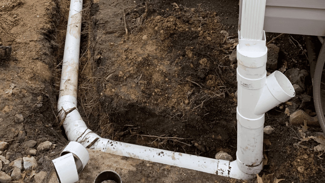 PVC drainage pipes installed in a trench with dirt and rocks, ensuring proper water flow.