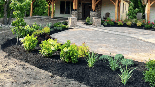 Beautifully landscaped garden with patio and stone accents, featuring colorful plants and mulch.