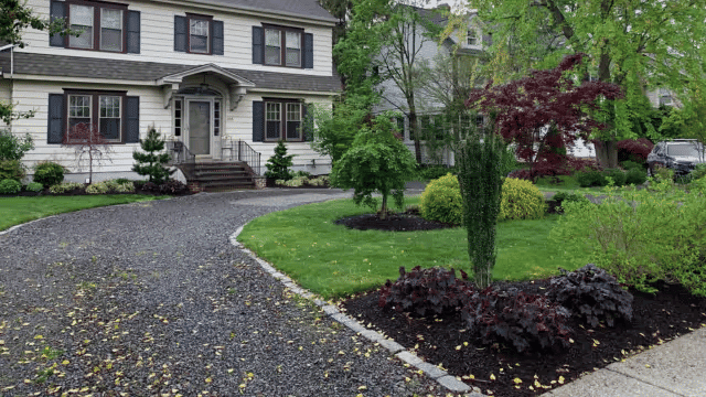 Well-manicured garden with a stone driveway and a charming two-story house.