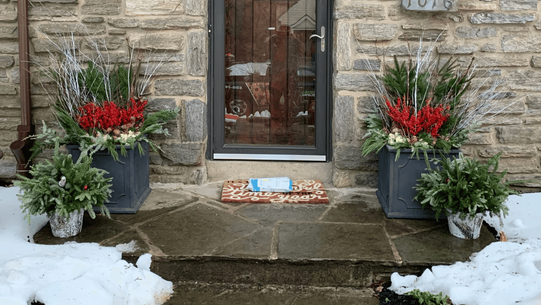 Winter entrance with stone walls, festive planters, and a decorated doormat.