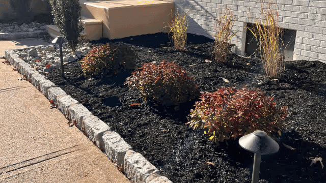 Beautifully landscaped front yard with flowering shrubs, decorative stones, and ambient lighting.