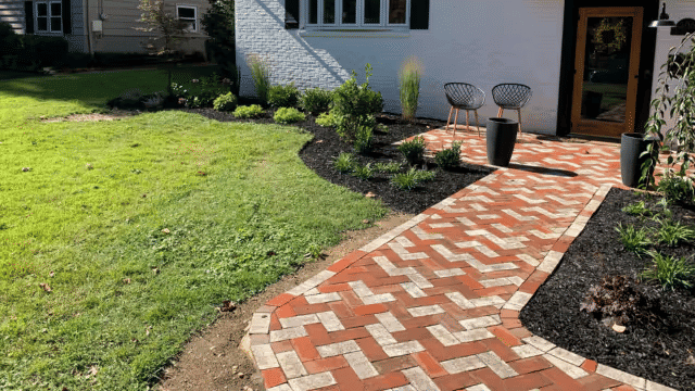 Brick pathway leading to a modern home entrance surrounded by landscaped greenery.