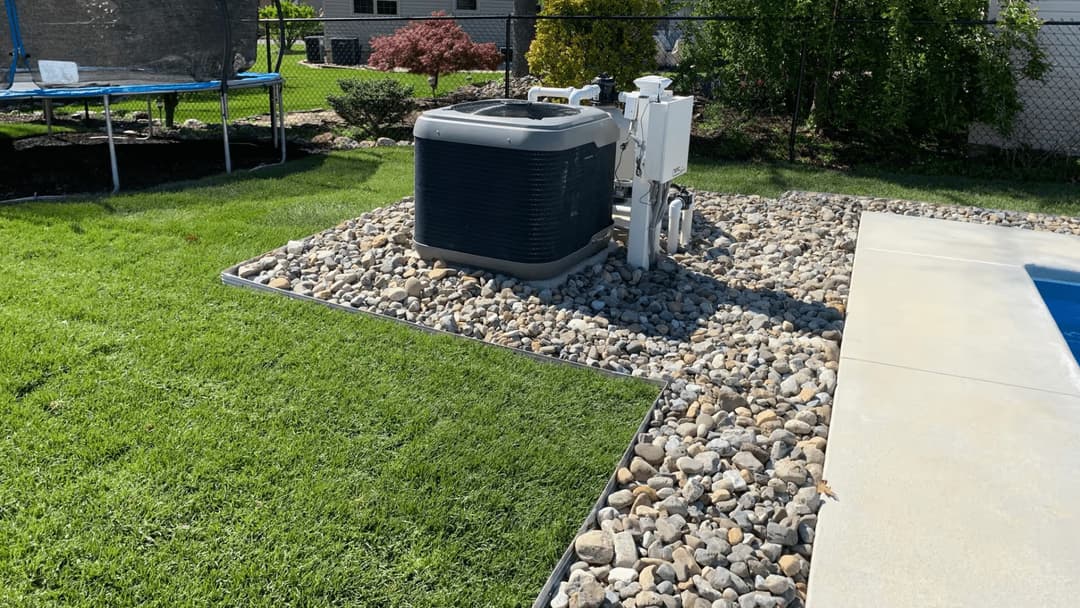 Swimming pool area featuring a heat pump surrounded by rocks and manicured grass.