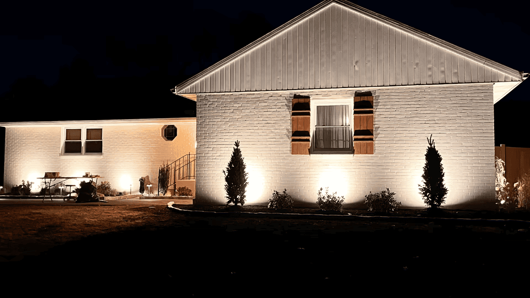 Illuminated suburban home at night with landscaped yard and decorative lighting.