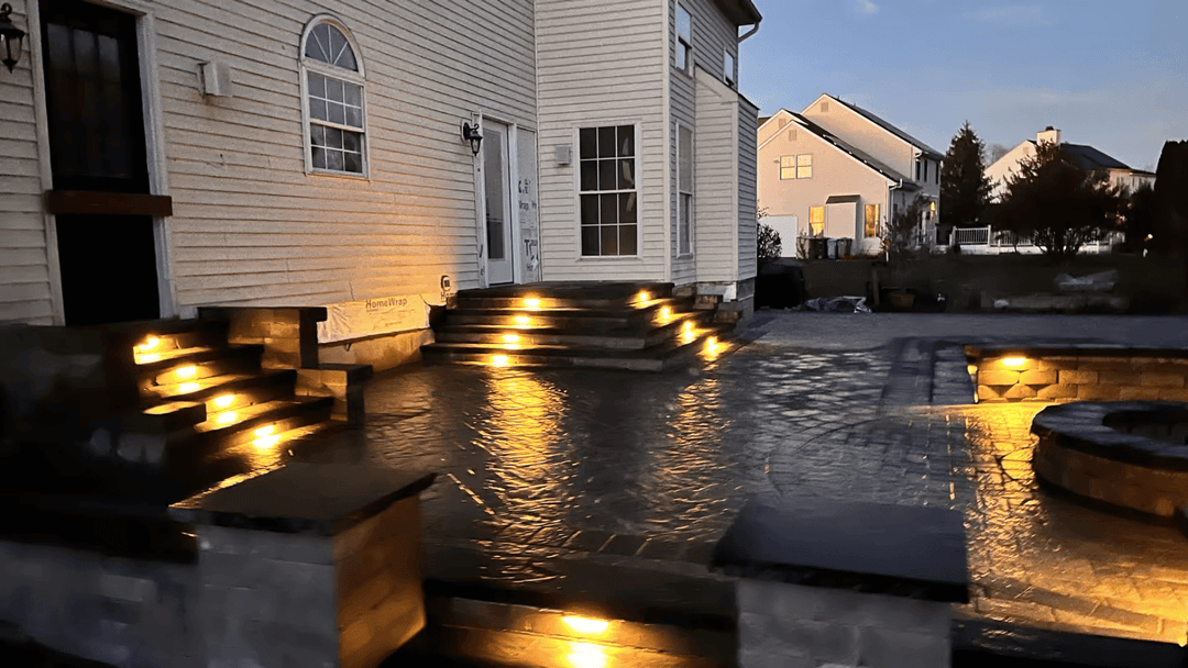 Exterior home with illuminated steps and patio, showcasing modern landscape lighting at dusk.