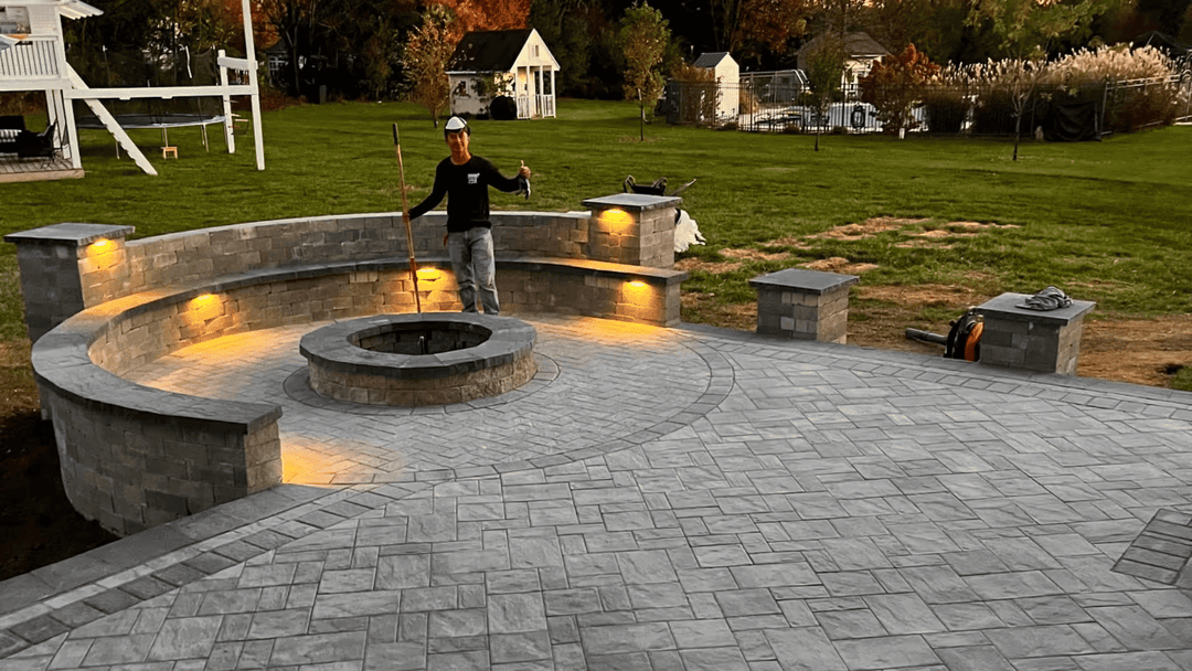 Patio with stone seating, fire pit, and ambient lighting; contractor showcasing completed project.