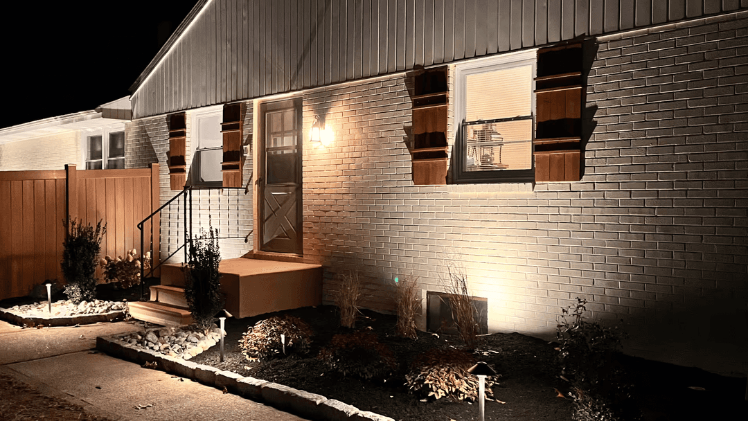 Well-lit modern home exterior at night with landscaped front yard and decorative lighting.