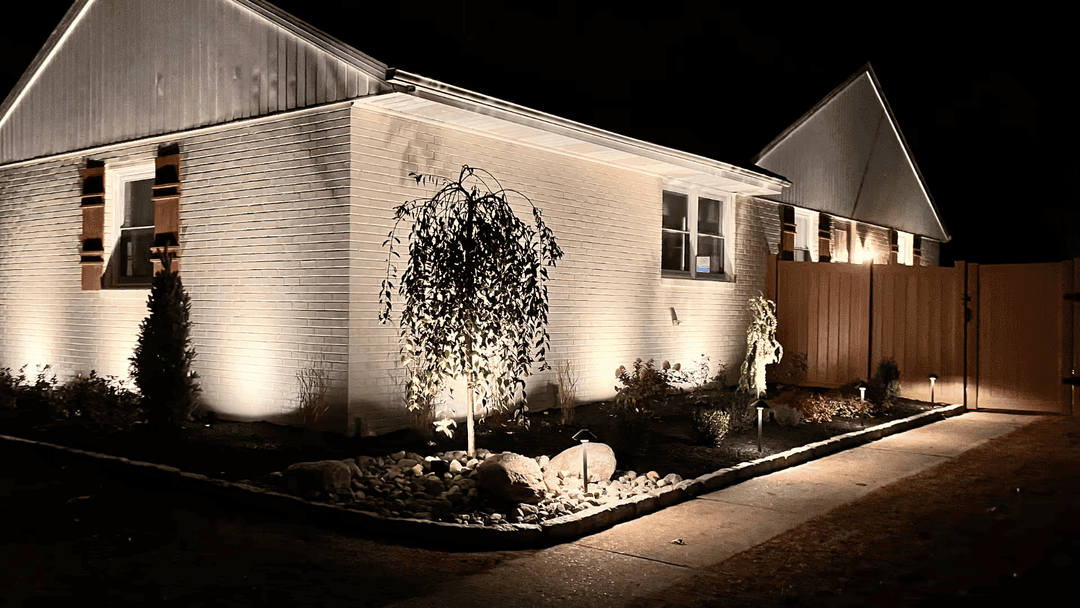 Illuminated exterior of a modern home at night featuring landscaped garden and fence.