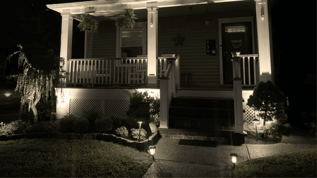 Charming illuminated house porch at night with welcoming landscaping and soft lighting.