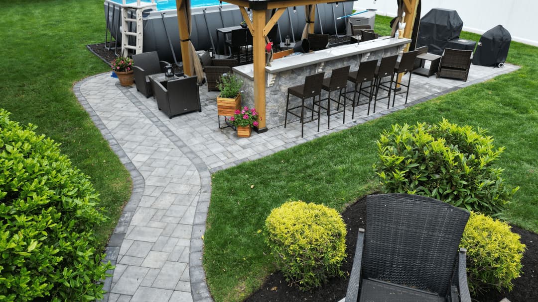 Outdoor patio with bar seating, stone path, and green landscaping near a pool.