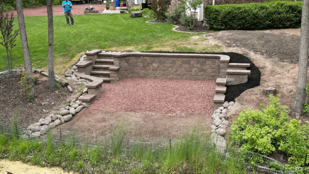 Landscaped backyard with stone retaining wall, steps, and gravel area for outdoor seating.