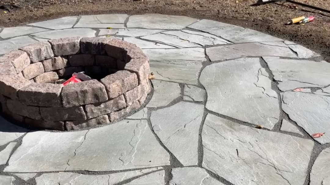 Stone fire pit surrounded by a circular flagstone patio in a garden setting.