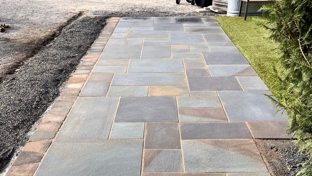 Paved stone walkway with rectangular stones and borders, surrounded by gravel and greenery.