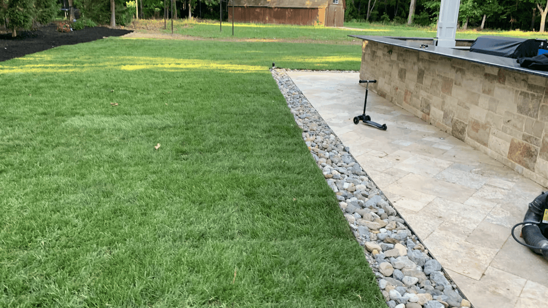 Lush green lawn with stone edging and a paved patio area in a landscaped yard.
