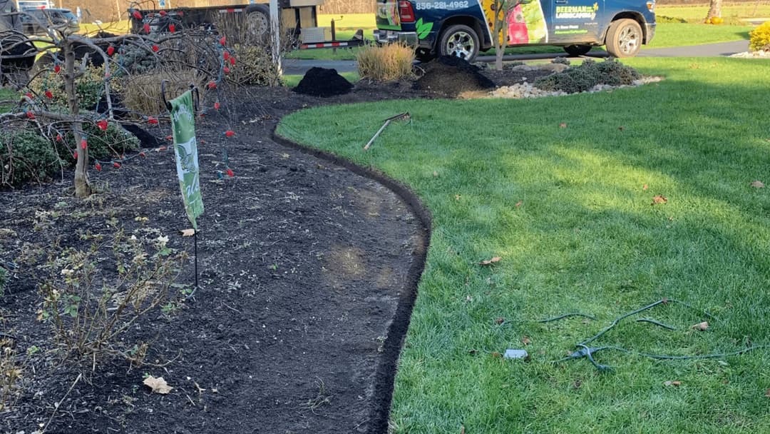 Lawn care and landscaping work in a residential yard with green grass and mulch outline.