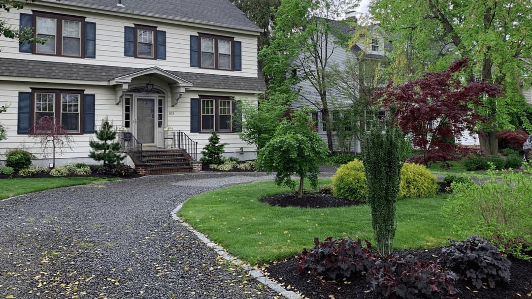 Charming two-story home with landscaped garden and gravel path in a residential neighborhood.