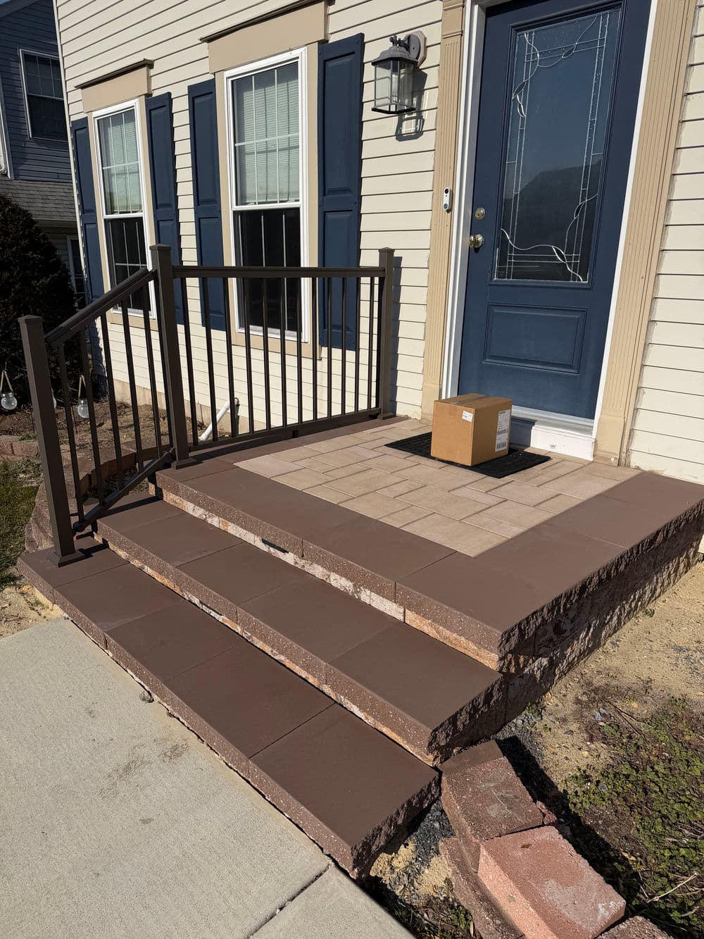 Newly designed front porch with stone steps, railing, and delivery box by the doorway.