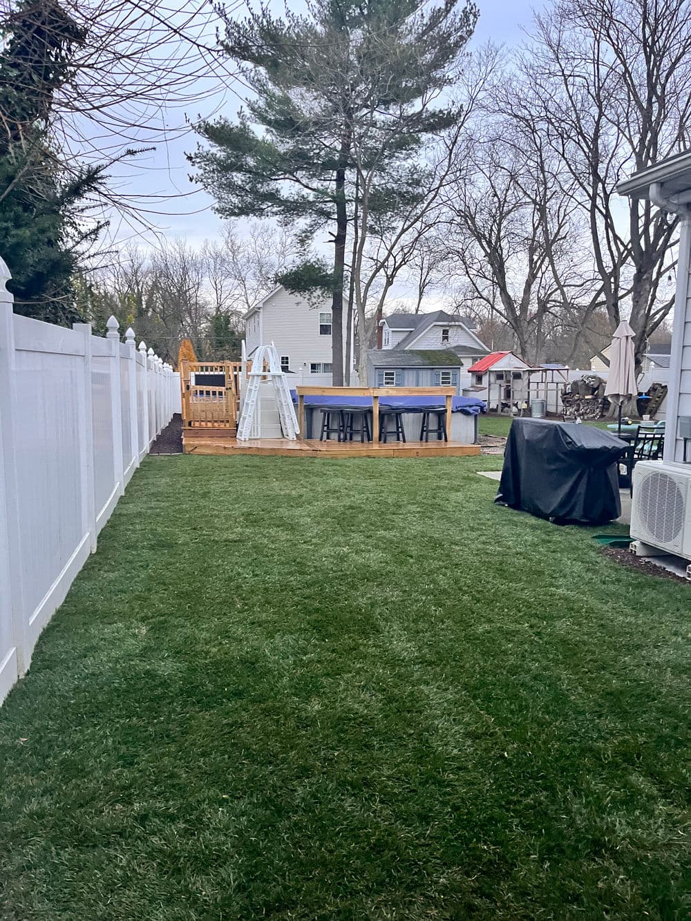 Lush green backyard with a wooden deck, outdoor seating, and a tall tree.