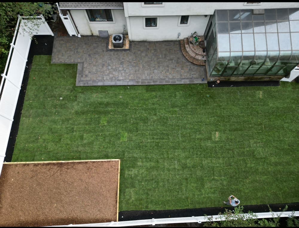 Aerial view of a backyard featuring a green lawn, patio, and greenhouse.