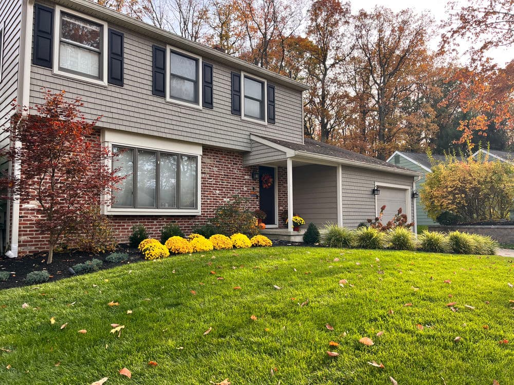 Charming two-story home with landscaped yard, autumn foliage, and vibrant yellow chrysanthemums.