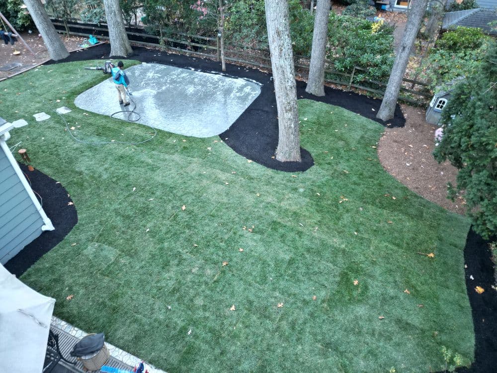 Landscape renovation with installed artificial turf and a worker preparing a patio area.