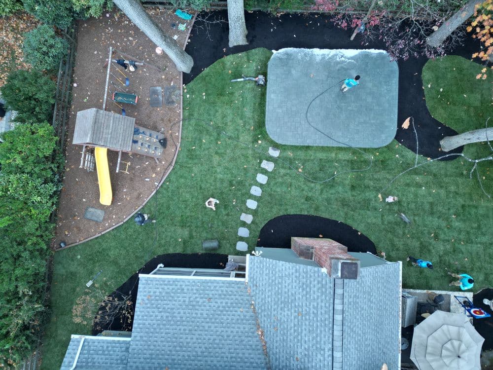 Aerial view of landscaped backyard with playground, patio, and workers installing sod.
