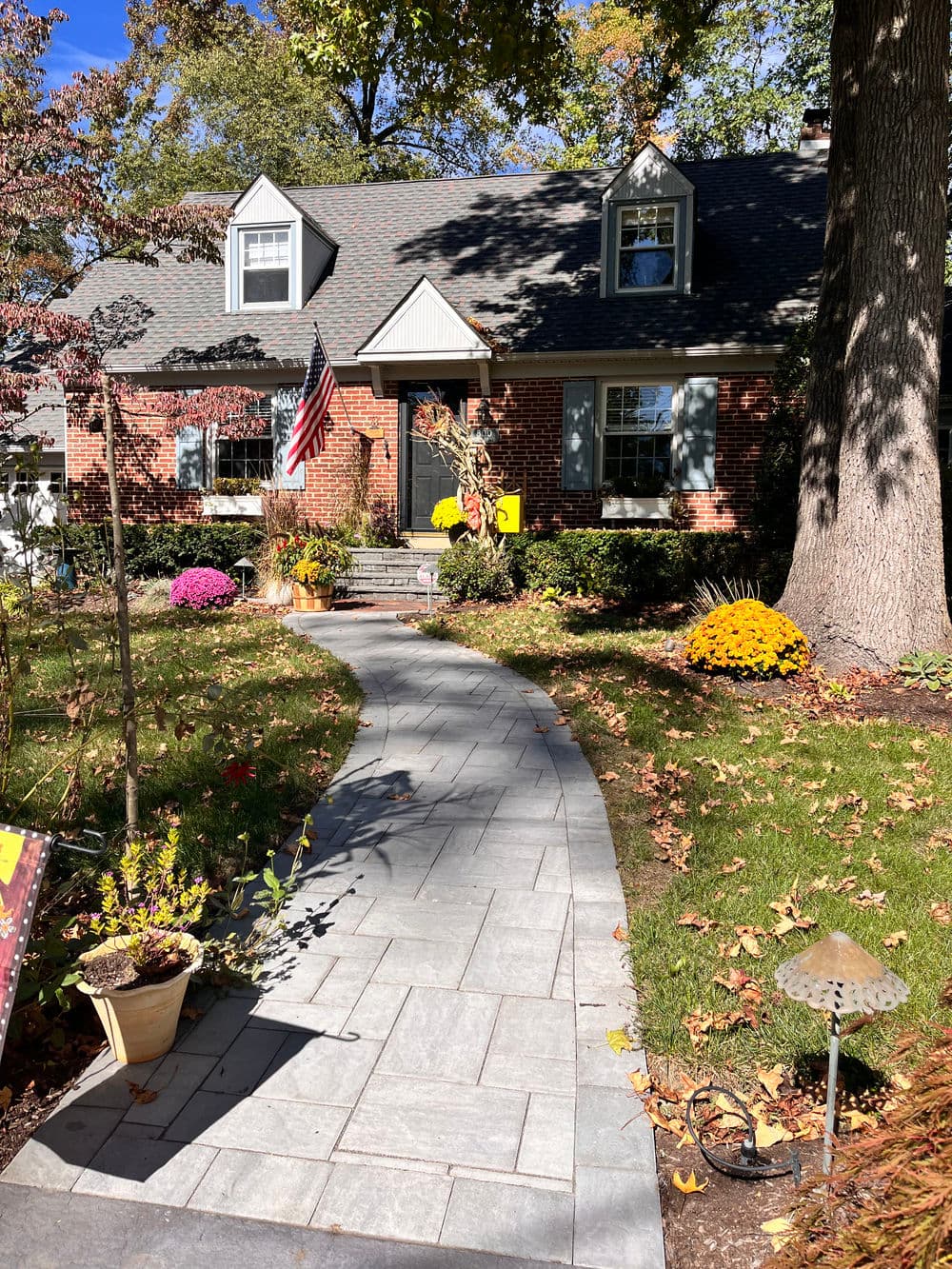 Charming brick house with American flag, colorful fall flowers, and stone pathway.