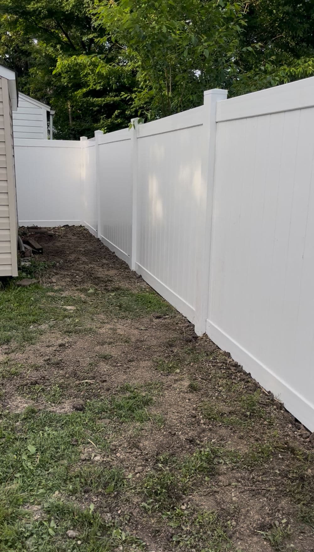 White vinyl fence along a garden path with sparse grass and dirt.