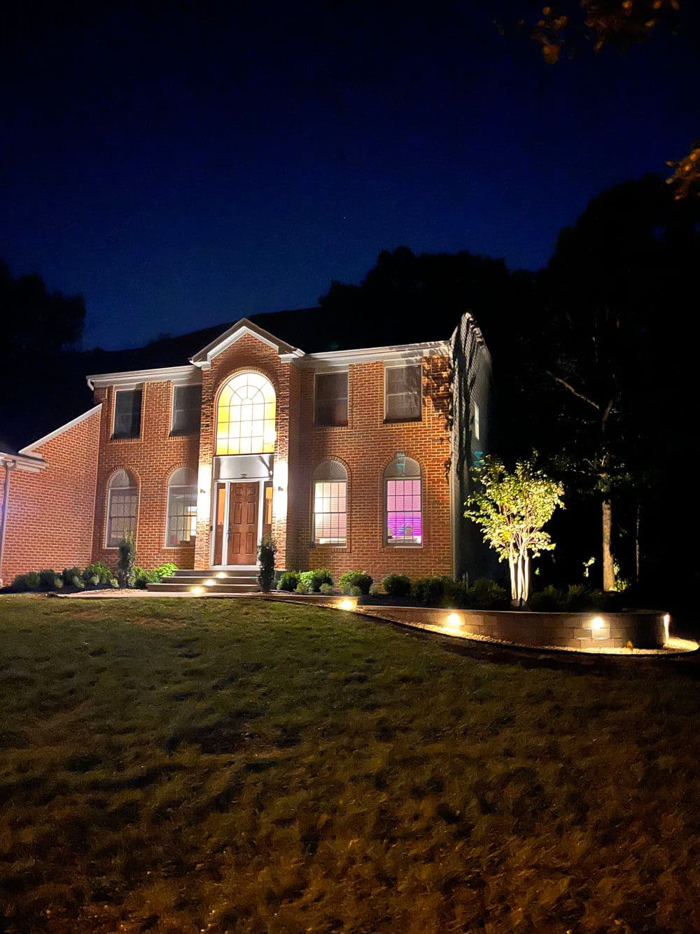 Elegant brick house at night with illuminated entryway and landscaped front yard.