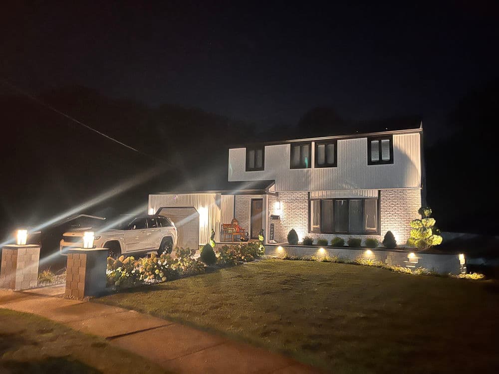 Two-story modern home illuminated at night with landscaped yard and driveway.
