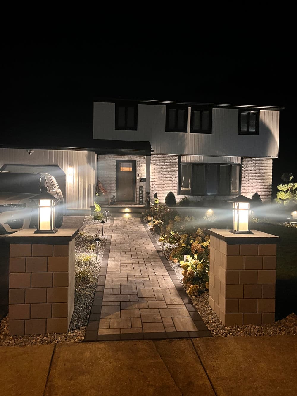 Modern two-story home at night with illuminated path and decorative landscaping.